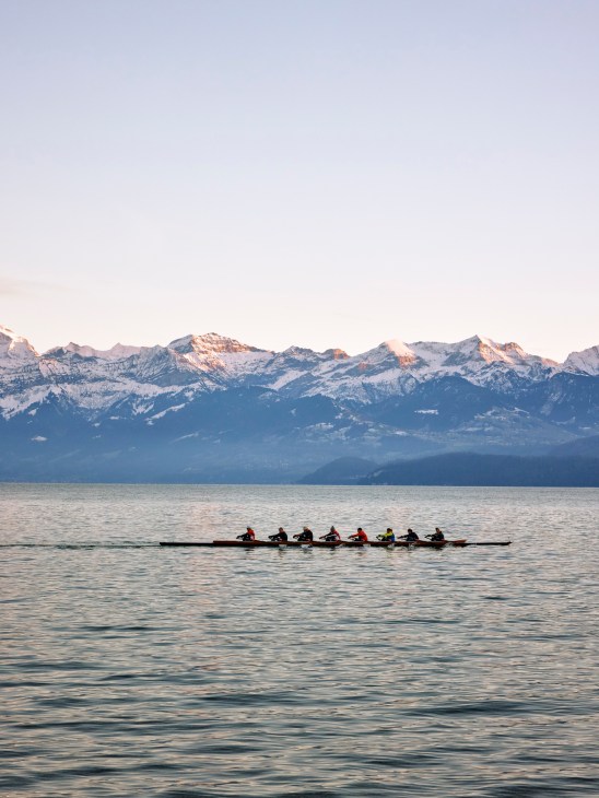 A group rowing on a lake with a mountain range in the background.