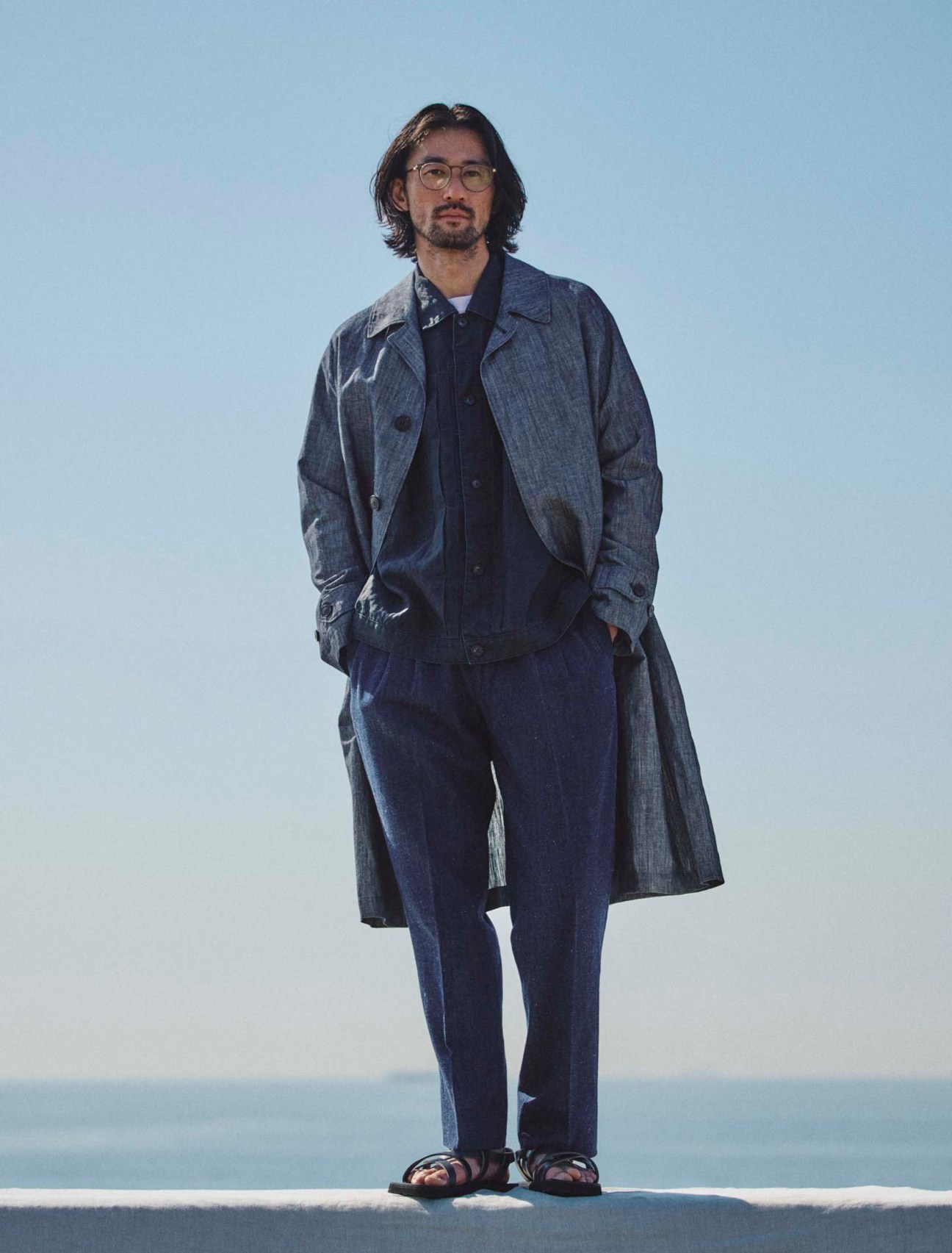 Coat by Hevò, jacket by Porter Classic, t-shirt by Comoli, trousers by Devorè Incipit, sandals by Hender Scheme, glasses by Mykita