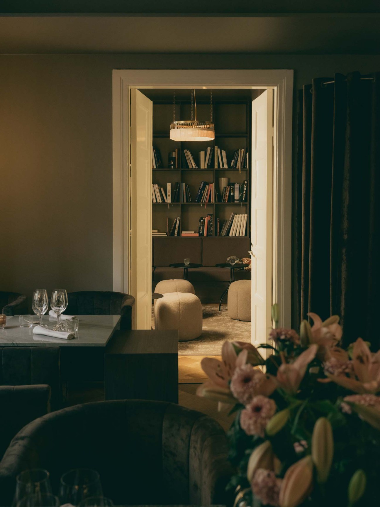 Cosy-looking restaurant space with flowers in the foreground and a reading room at the end of the picture