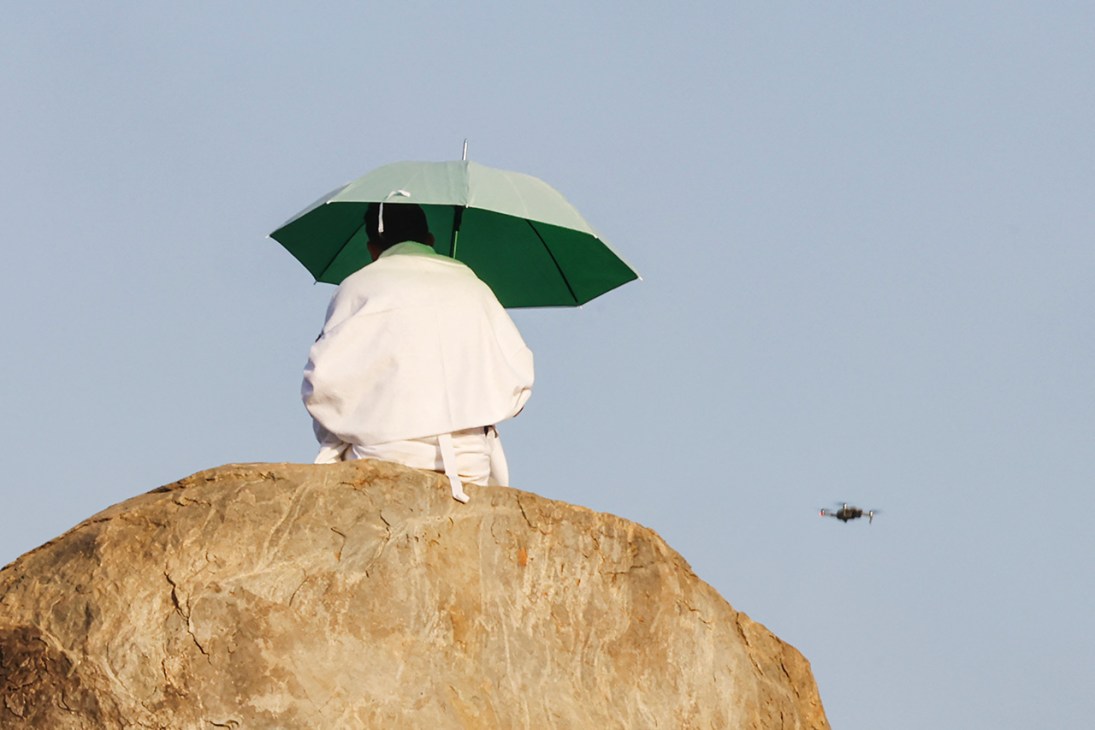 A surveillance drone flies past a praying Hajj pilgrim