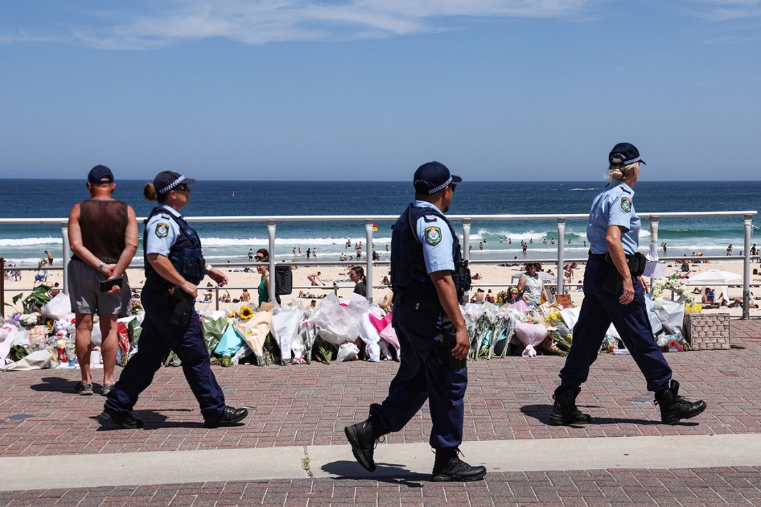 The Police walk past floral tributes left at the promenade of Bondi Beach in Sydney on December 18, 2025, to honour victims of the shooting that took place there on December 14. The attack at Bondi Beach on December 14 was one of the deadliest in Australian history. (Photo by DAVID GRAY / AFP via Getty Images)