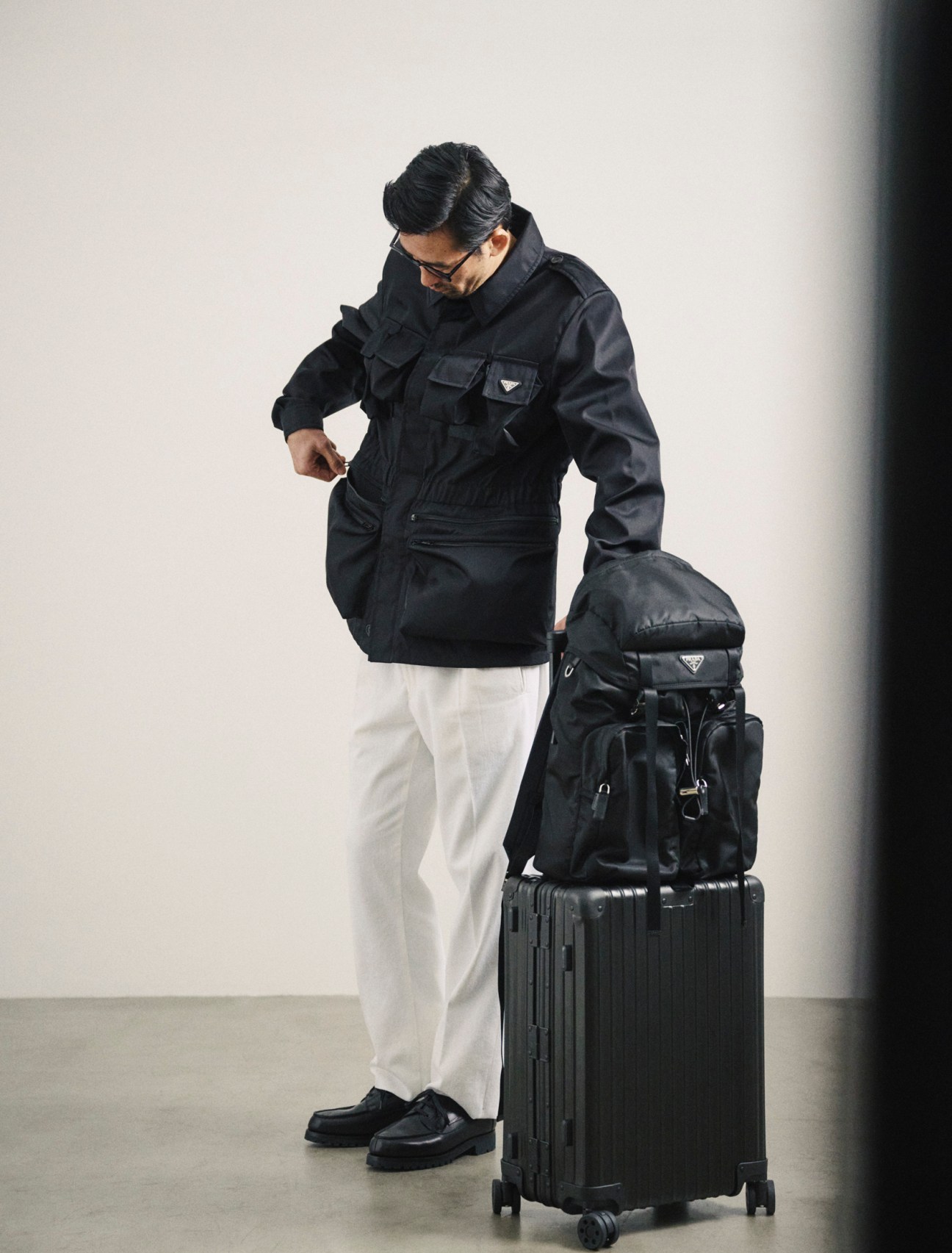 Jacket and backpack by Prada, trousers by Incotex, shoes by JM Weston, glasses by Mykita, suitcase by Rimowa