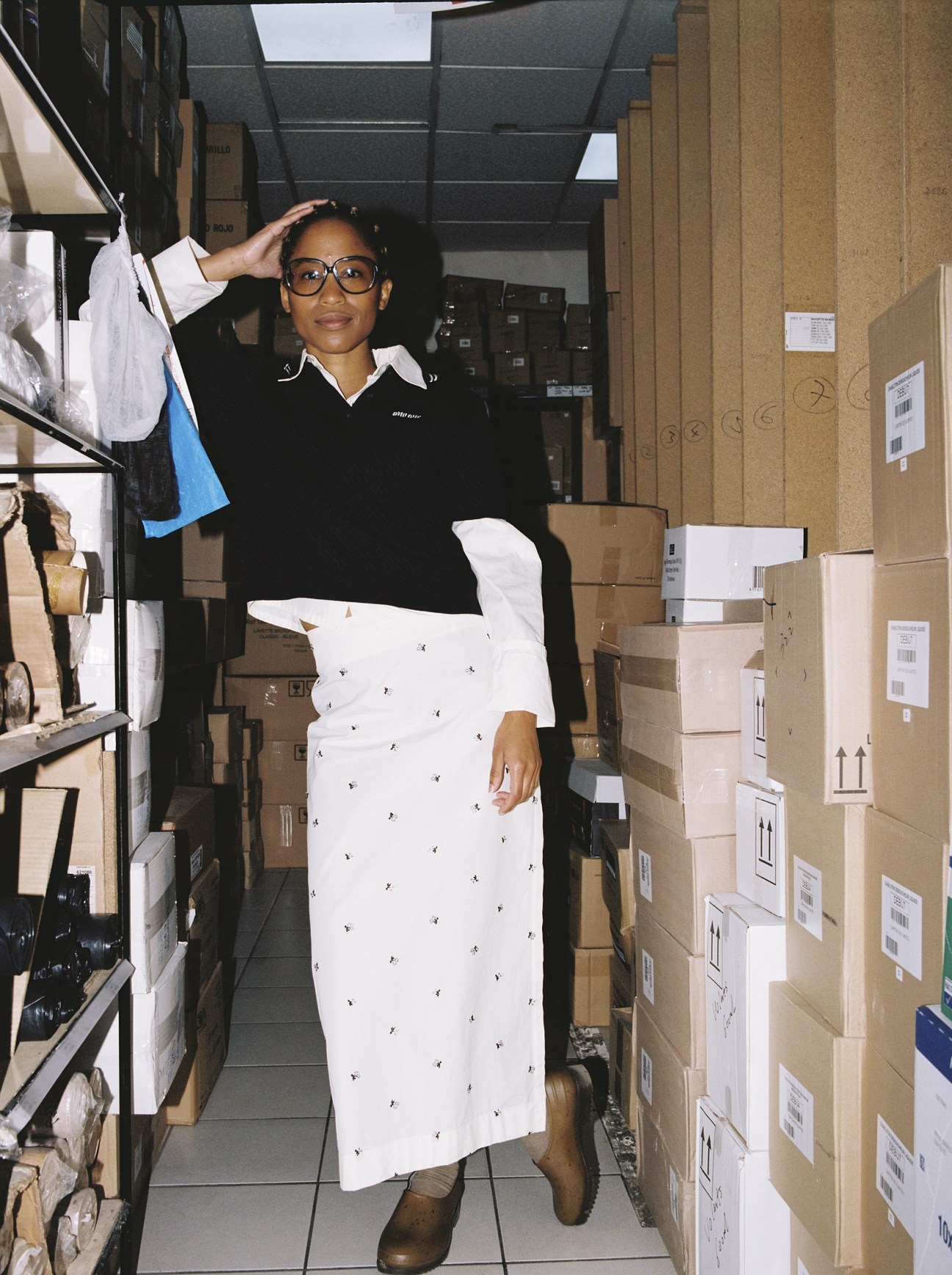 Zélikha Dinga wears jumper by Miu Miu, shirt and skirt by Rier, socks by Falke, shoes by Magasin Vivant!, glasses model’s own