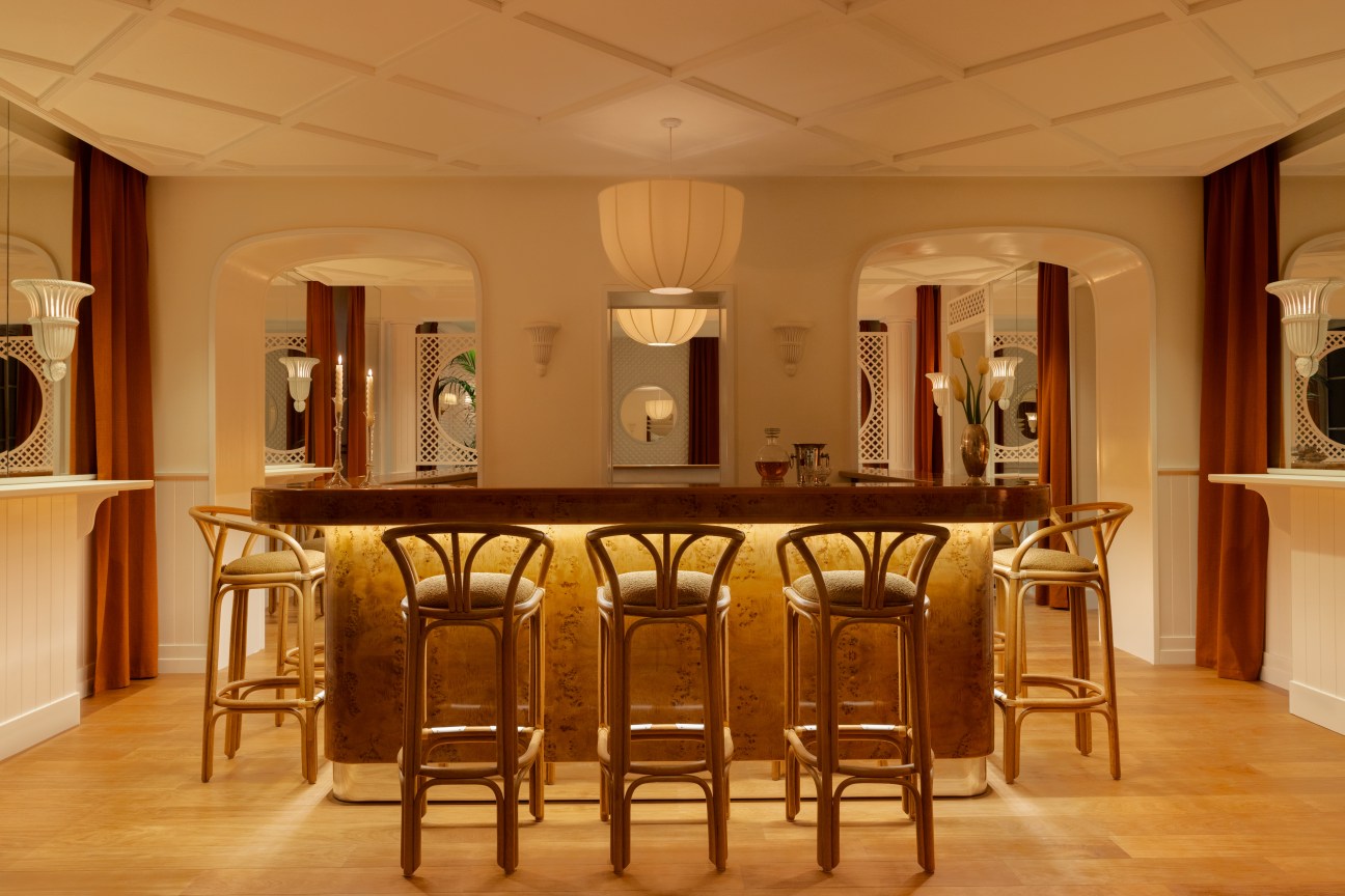 Hotel Lilou Bar minimalist polished wood bar between two archways with burnt orange drapes ratan barstools art deco white lampshades and mirrors